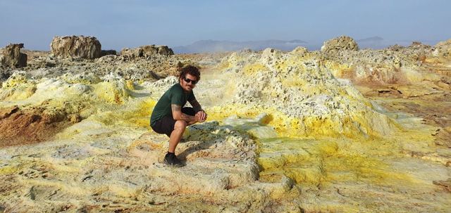 A man crouching among yellow and green sulphur formations at Dallol.
