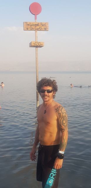 A man in sunglasses standing in the Dead Sea beside a post marking minus 430 metres.