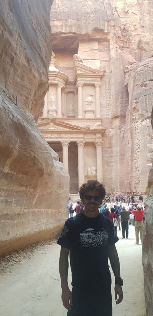 A man in sunglasses taking a selfie in the Siq with Petra's Treasury behind him.
