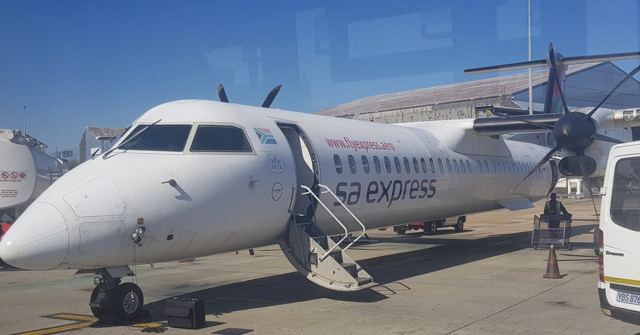 A white propeller plane with steps down on an airport apron.