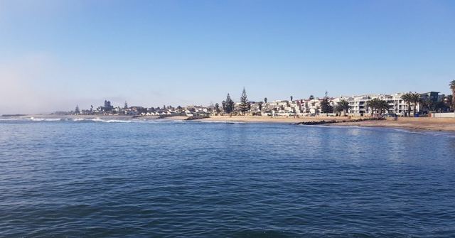 Calm blue sea with a low coastal town along the shore.