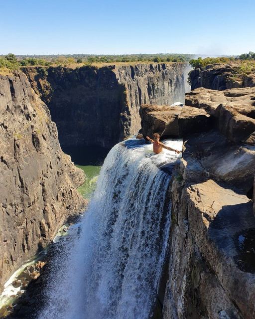 A person sitting in a rock pool at the very edge of Victoria Falls above a deep gorge.