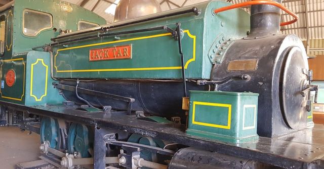 A green vintage steam locomotive with yellow lining in a museum shed.
