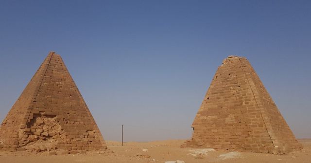 Two weathered stone pyramids against a deep blue sky.