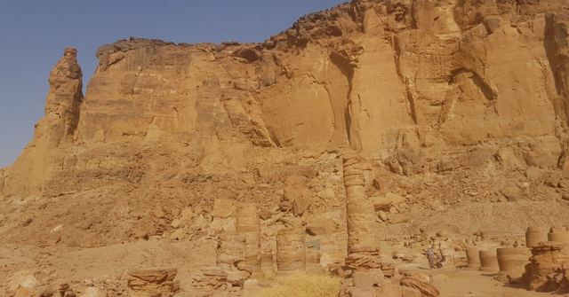 A sunlit sandstone cliff with a tall pinnacle at one end.