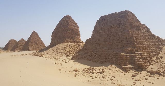Several weathered pyramids on pale sand under a hazy sky.