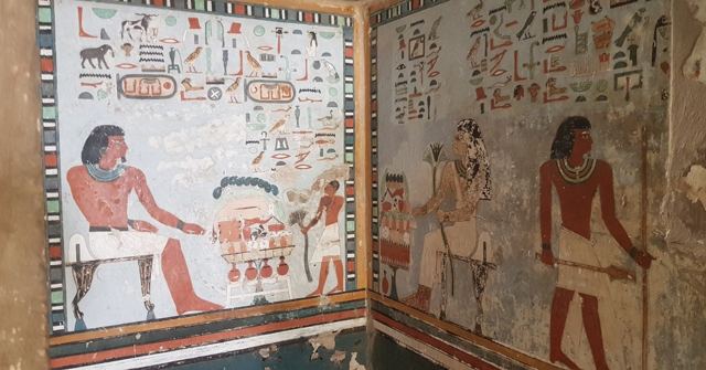Brightly painted ancient Egyptian tomb walls showing seated figures, offerings and hieroglyphs.
