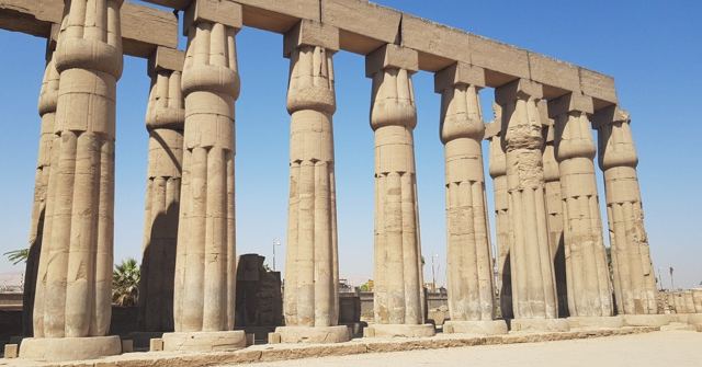 A long double row of tall sandstone papyrus columns under a clear blue sky.