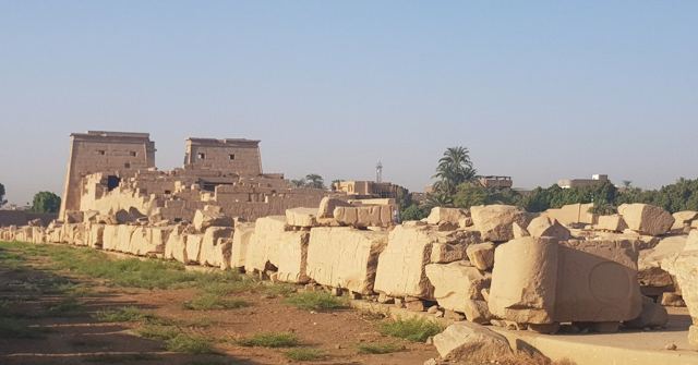 Rows of fallen sandstone blocks in front of distant temple pylons in soft evening light.