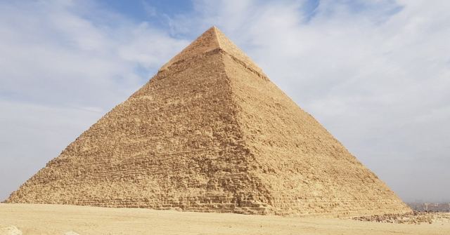 A great stone pyramid at Giza rising against a pale blue sky with light clouds.