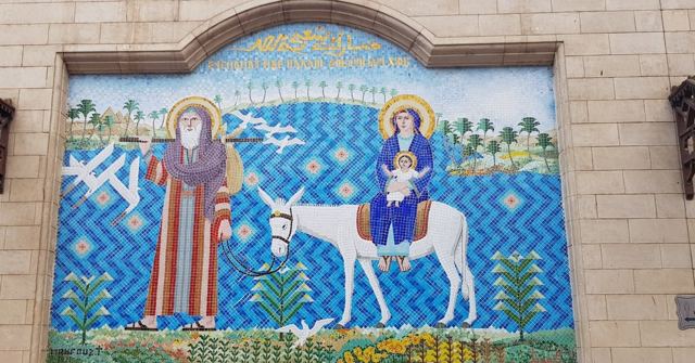 Wall mosaic showing a man leading a donkey carrying a woman and child beside the Nile.