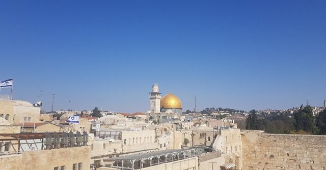 View over Jerusalem Old City rooftops towards the golden Dome of the Rock under blue sky.