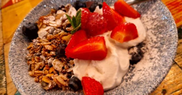 A bowl of granola topped with yoghurt and fresh strawberries on a wooden table.