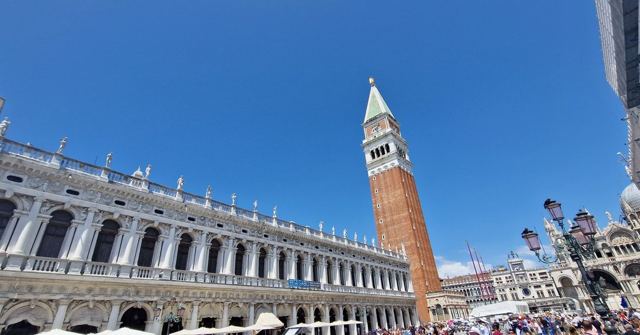 The tall brick bell tower in St Mark's Square beside ornate arcaded buildings under a blue sky.
