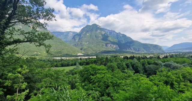 A green valley with jagged mountains rising behind it under blue sky and white clouds.