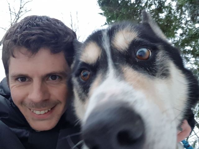 A man taking a close-up selfie with a husky in the snow.