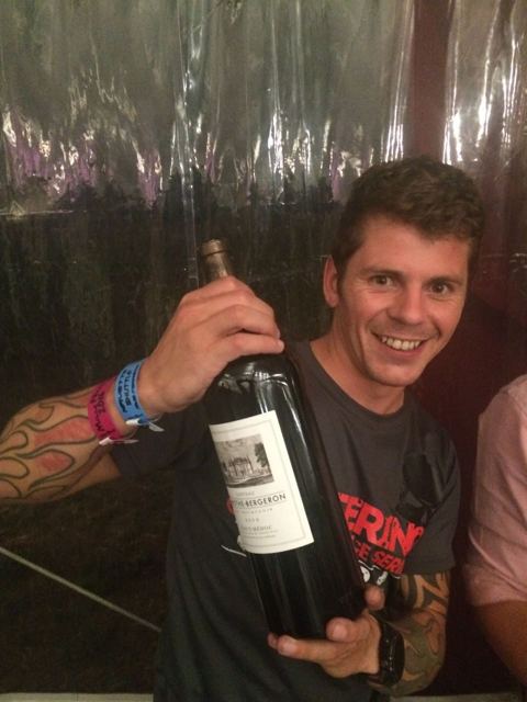 A smiling man in a running top holding a large bottle of red wine.