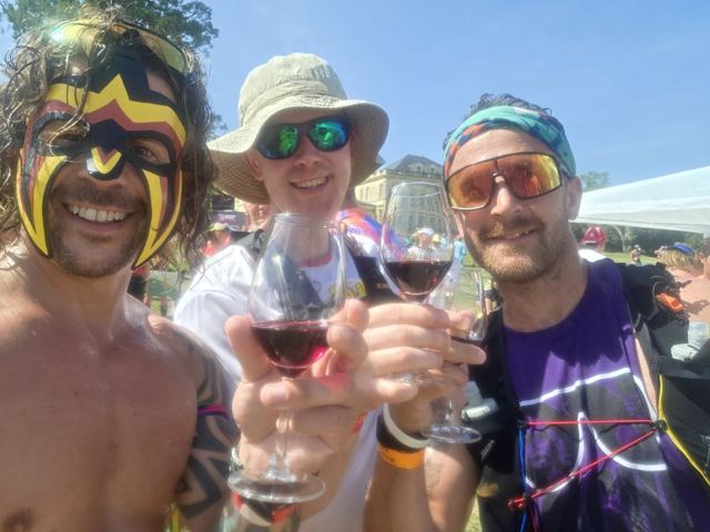 Three runners in costume raising glasses of red wine and smiling.
