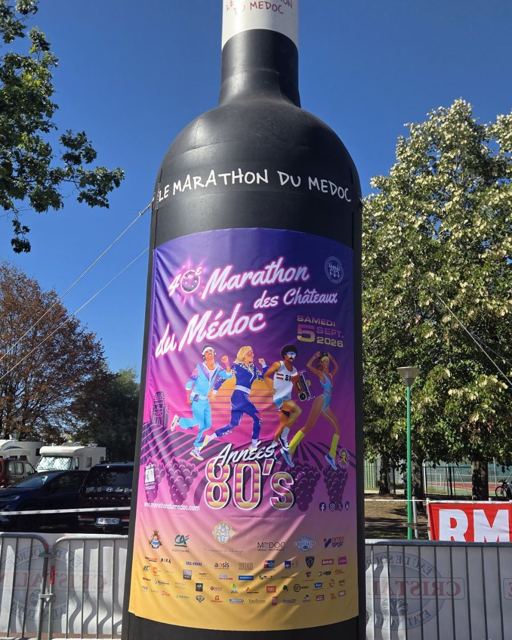 An enormous inflatable wine bottle with a Marathon du Médoc label against a blue sky.