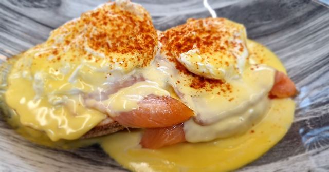 Eggs Benedict on smoked salmon covered in hollandaise and paprika on a dark plate.