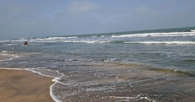 Waves rolling onto a wide sandy beach under a grey-blue sky.
