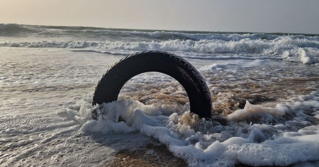 A half-buried tyre on the shoreline with white foam from breaking waves around it.