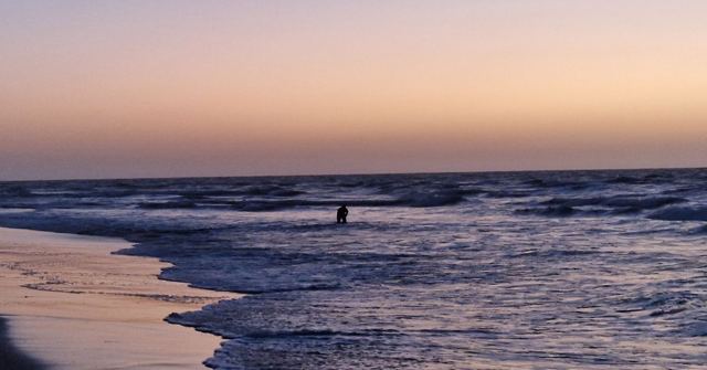 Waves washing onto a beach under a soft pink and orange sky at dusk.
