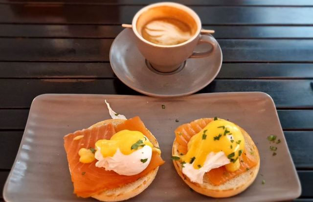 Two smoked salmon eggs Benedict on a rectangular plate beside a cup of flat white coffee.