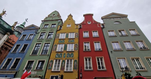 Tall colourful gabled townhouses in green, red and yellow against a grey sky.