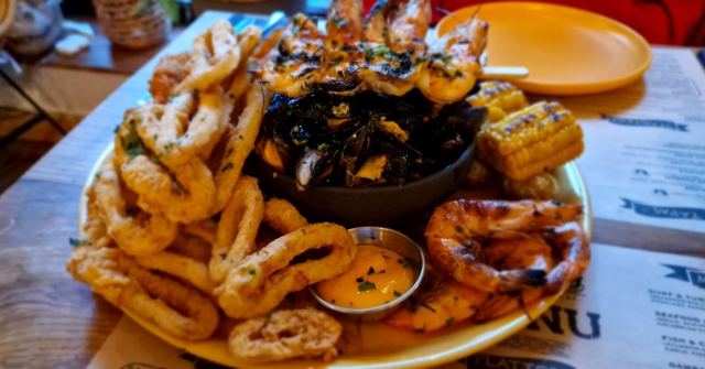 A platter of fried calamari rings, mussels, prawns and corn on the cob on a wooden table.