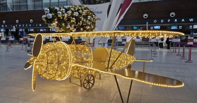 An illuminated wire biplane decoration in an airport departures hall with a Christmas tree behind.