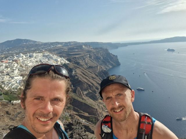 Two runners taking a selfie on a clifftop trail above the caldera of Santorini.