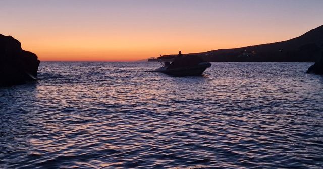Calm water reflecting an orange sunset sky, with dark rocky cliffs on either side.