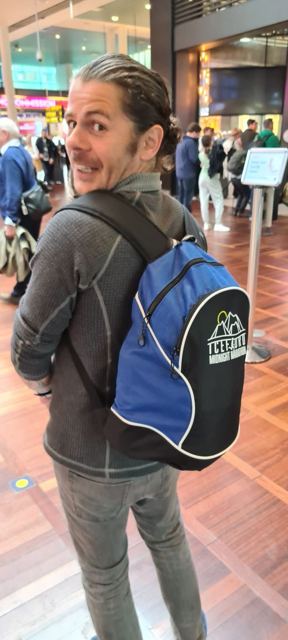 A man with a race backpack looking back over his shoulder in an airport terminal.