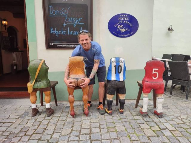 A man sitting on a bench among carved wooden figures outside a hotel.