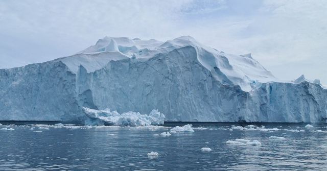 A huge white iceberg with sheer sides floating in calm grey-blue water.