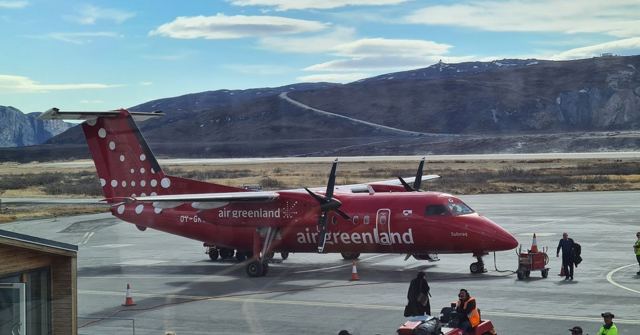 A red Air Greenland propeller plane on the airport tarmac with brown mountains behind.