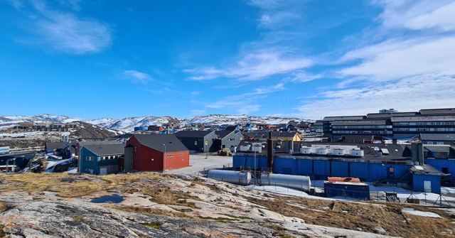 Colourful wooden houses spread across rocky ground with snow-covered hills behind.