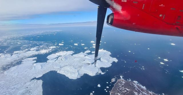 A red aircraft propeller with sea ice and icebergs on a dark blue sea far below.
