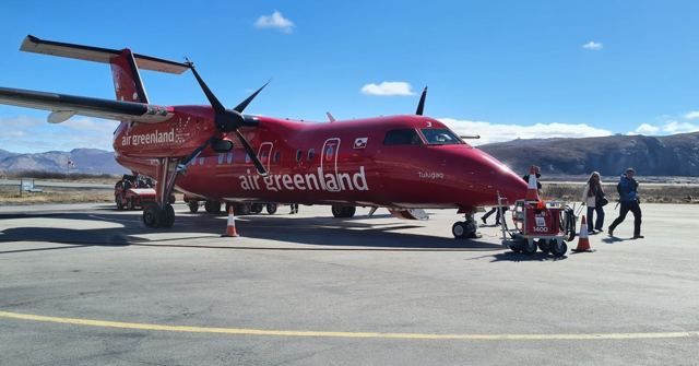 A red Air Greenland propeller plane on the tarmac with passengers walking nearby.