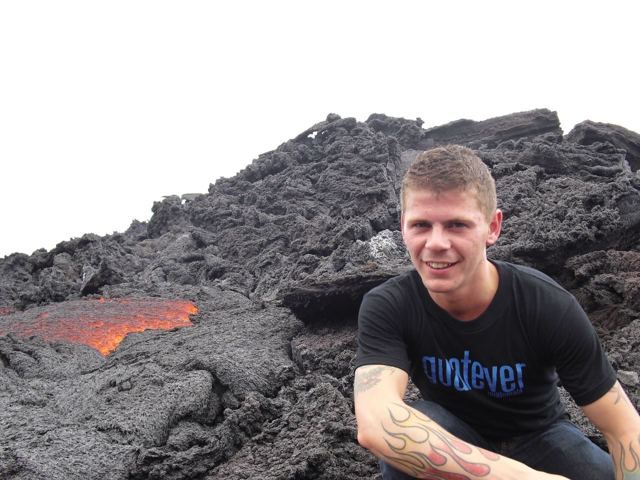 A man sitting on black volcanic rock beside a glowing orange lava flow on Pacaya.