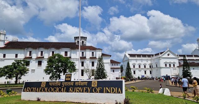 Large white colonial church buildings behind a lawn and an Archaeological Survey of India sign.