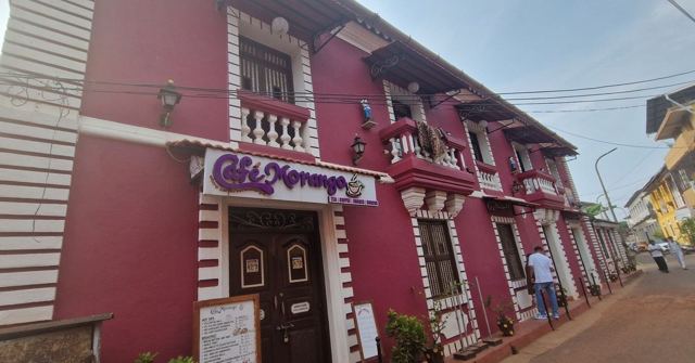A deep red two-storey colonial building with white window frames and balconies on a street.