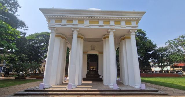A white neoclassical pavilion with tall columns, surrounded by trees and lawn.