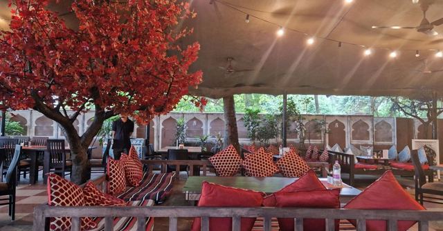 A restaurant interior with red cushioned seating, warm lights and a tree with red leaves.