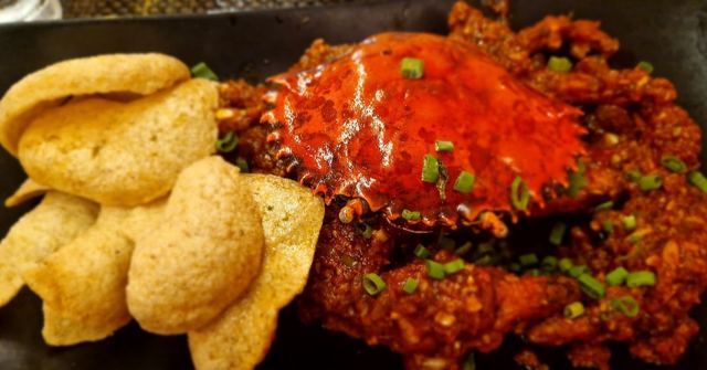 A whole crab in thick red masala sauce served with crispy poppadoms on a dark plate.