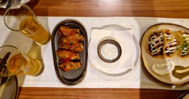 Glasses of beer next to plates of grilled skewers, a dip and loaded flatbreads on a table.