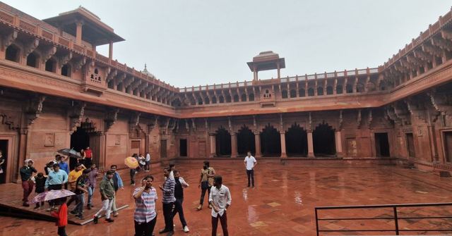A large red sandstone courtyard with arched galleries and visitors walking across it.