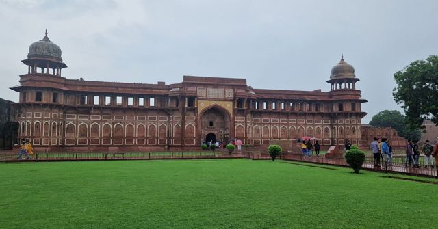 A long red sandstone palace with domed pavilions behind a neatly mown green lawn.