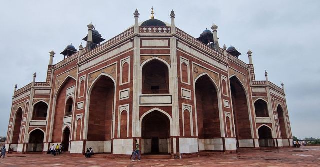 The red sandstone and white marble Humayun's Tomb with large arches under a cloudy sky.